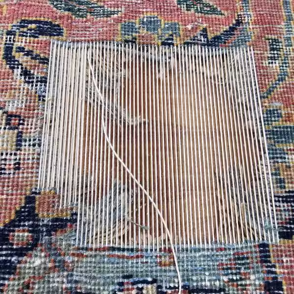 Artisan performing detailed hand reweaving on antique rug restoring structural integrity in Auckland workshop