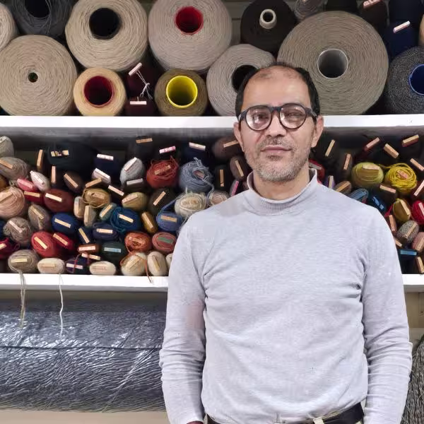Hamid, master rug restorer at The Rug Guru Auckland, working in a rug restoration workshop surrounded by yarns and textile materials used for handmade rug repair