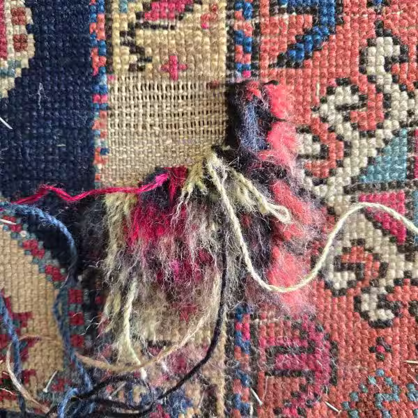 Close-up artisan hand reweaving Persian rug restoring missing fibres and knot structure in Auckland workshop