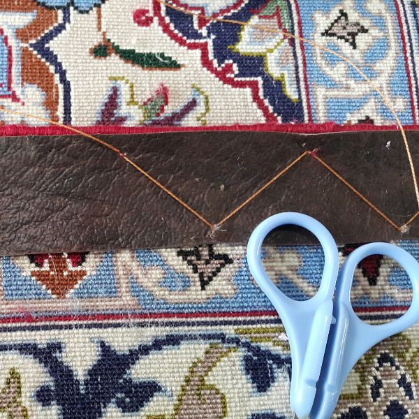 Finished rug edge after leather backing applied showing flat, stable and reinforced border