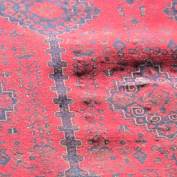 Loose rug with ripples and lifting areas creating trip hazards before repair