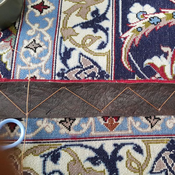 Curled rug edge before leather reinforcement showing structural instability and lifting border