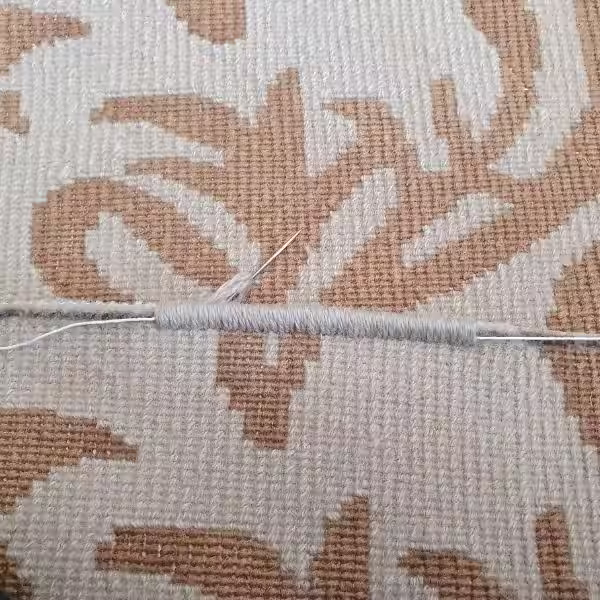 Rug technician reinforcing handmade rug perimeter using traditional hand binding technique for durability