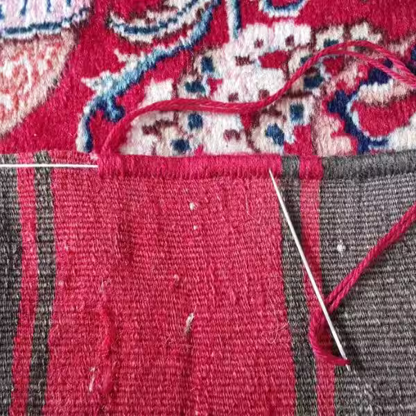 Close-up of hand-stitched rug edge binding process reinforcing handmade wool rug borders